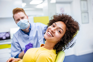 Smiling patient smiles at the camera while her dentist prepares for her dental exam